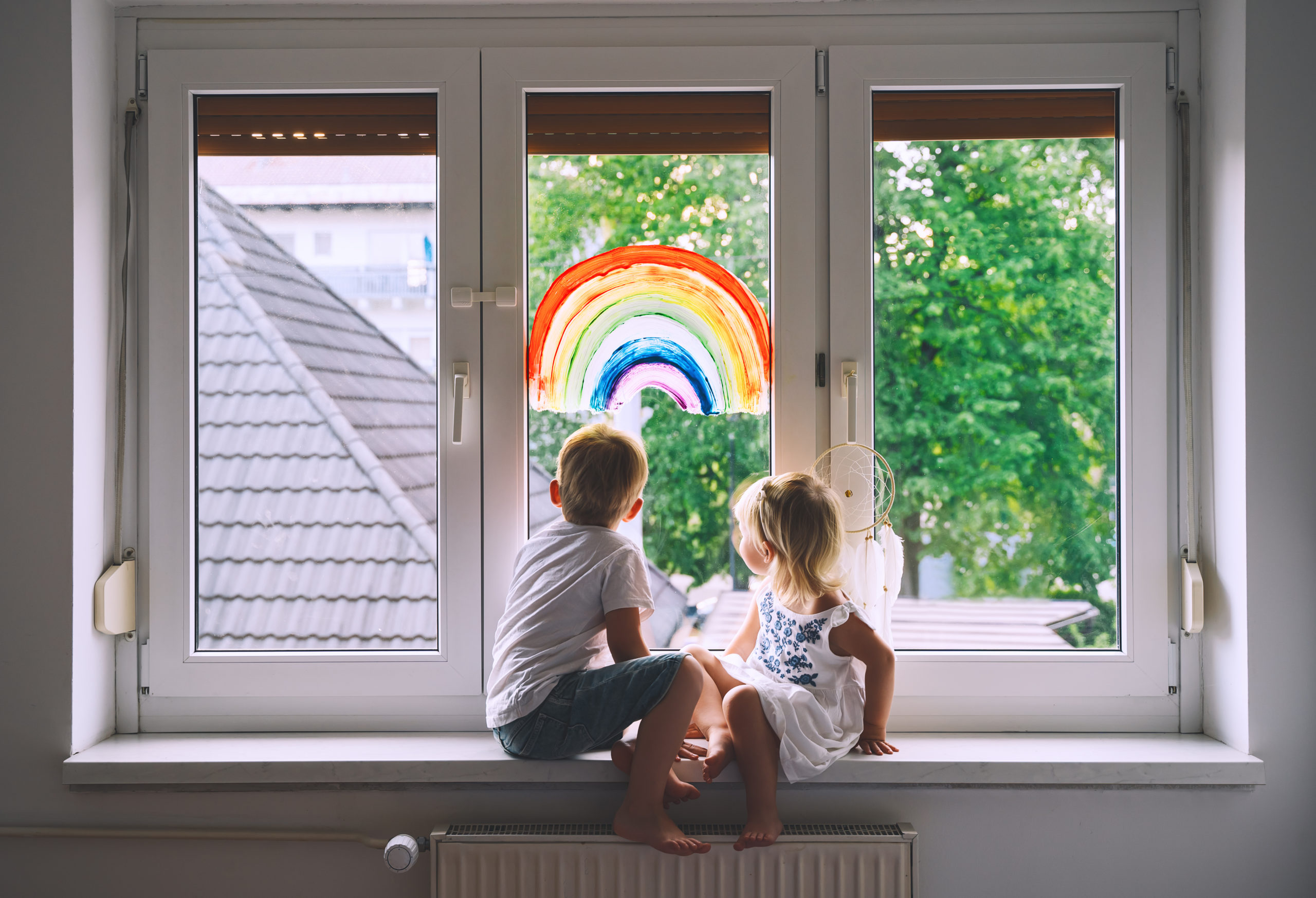 Zwei Kinder sitzen an einem Fenster mit Regenbogen